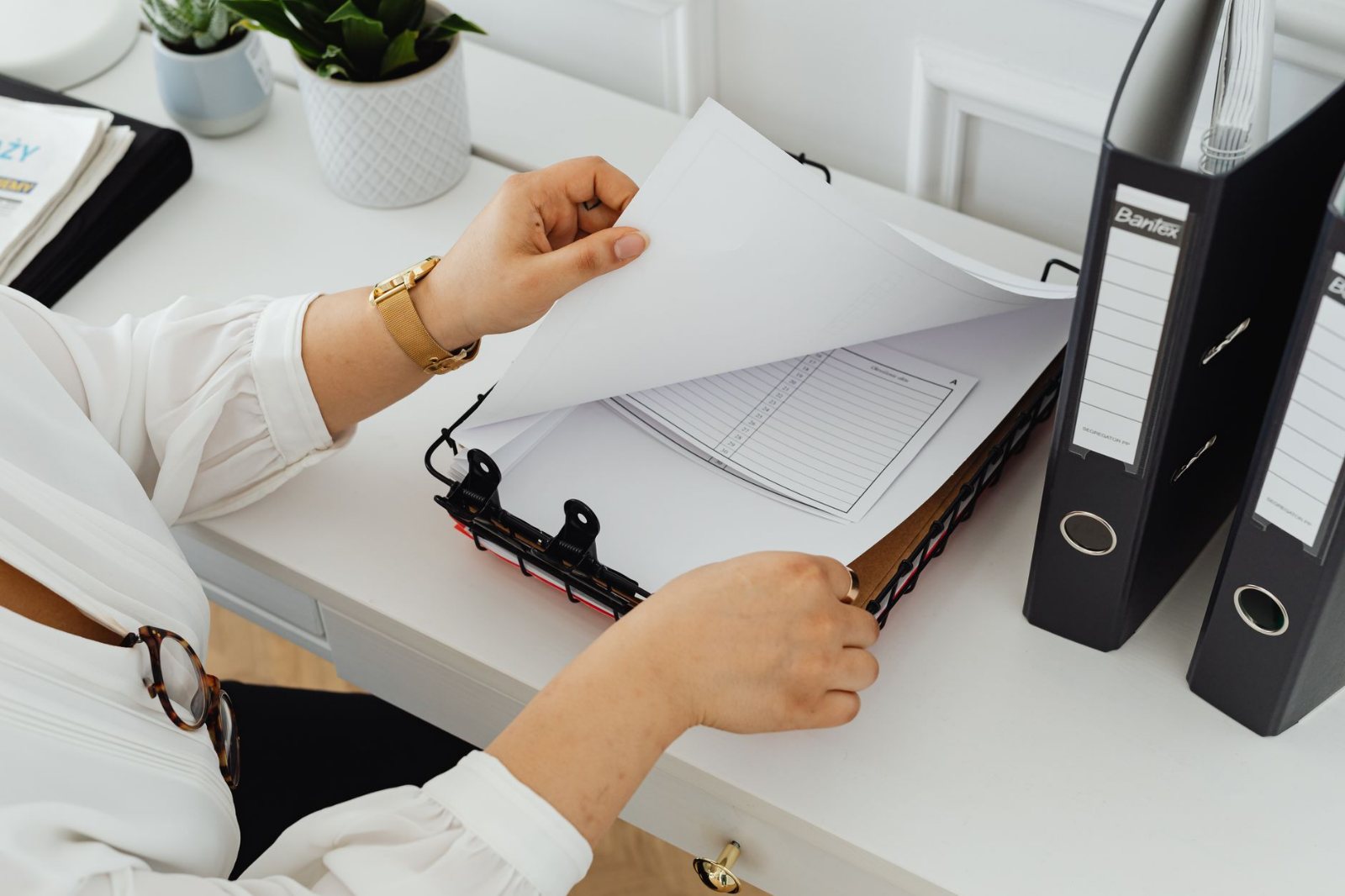 A hand sliding a tabbed document into a labeled ring binder on a small business back-office counter, other binders standing upright behind it